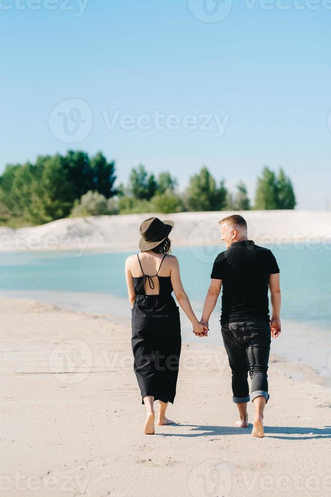 jovem casal um cara com uma garota em roupas pretas está andando na areia branca foto