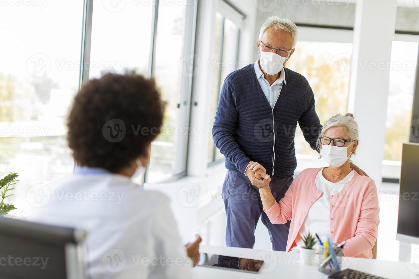 casal maduro falando com um médico usando máscaras foto