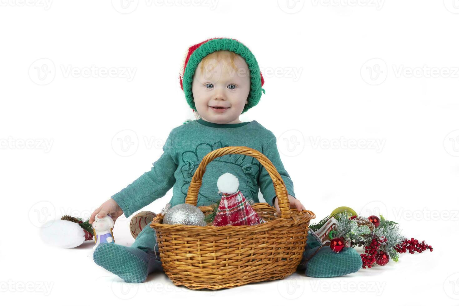 uma lindo Natal criança com uma cesta preenchidas com Natal brinquedos parece às a Câmera e sorrisos em uma branco fundo. engraçado Garoto com Natal árvore decorações. foto