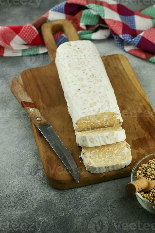 cru tempeh ou tempero, tempeh fatias em de madeira prato e cru soja sementes. tempe é uma tradicional indonésio Comida fez a partir de fermentado soja. foto