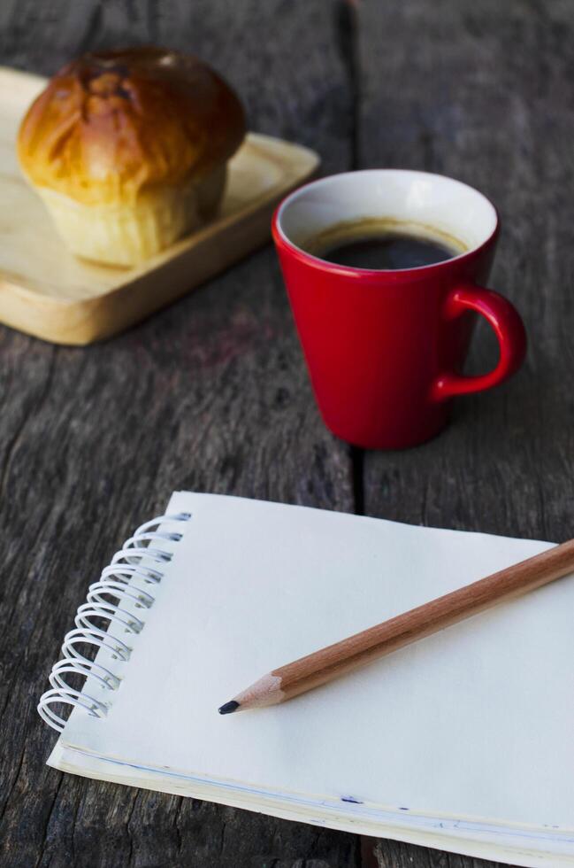 feche o lápis com o bloco de notas e a xícara de café vermelha no fundo da mesa de madeira foto