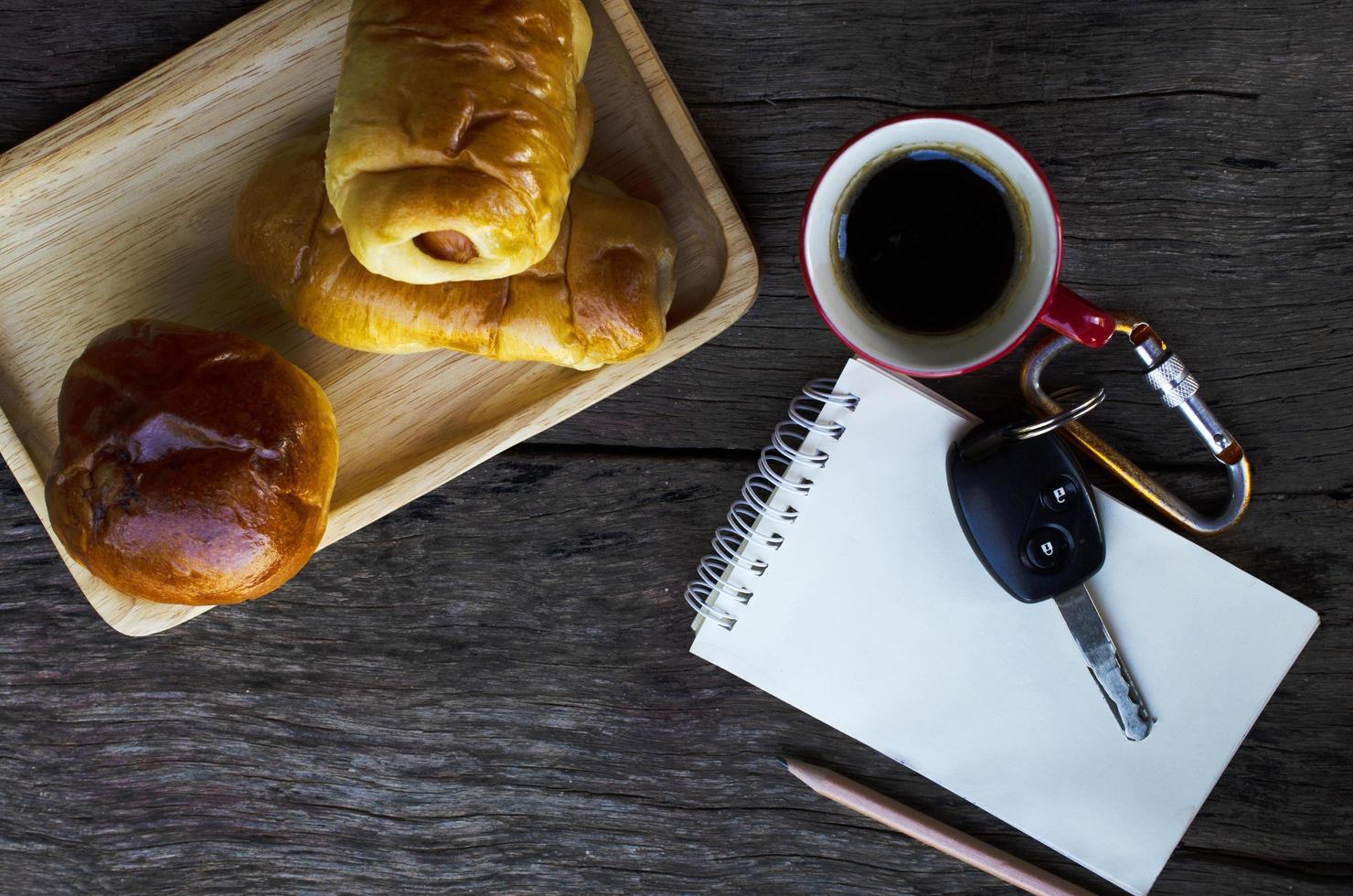 xícara de café vermelha e chave do carro e pãezinhos saborosos no fundo da mesa de madeira foto