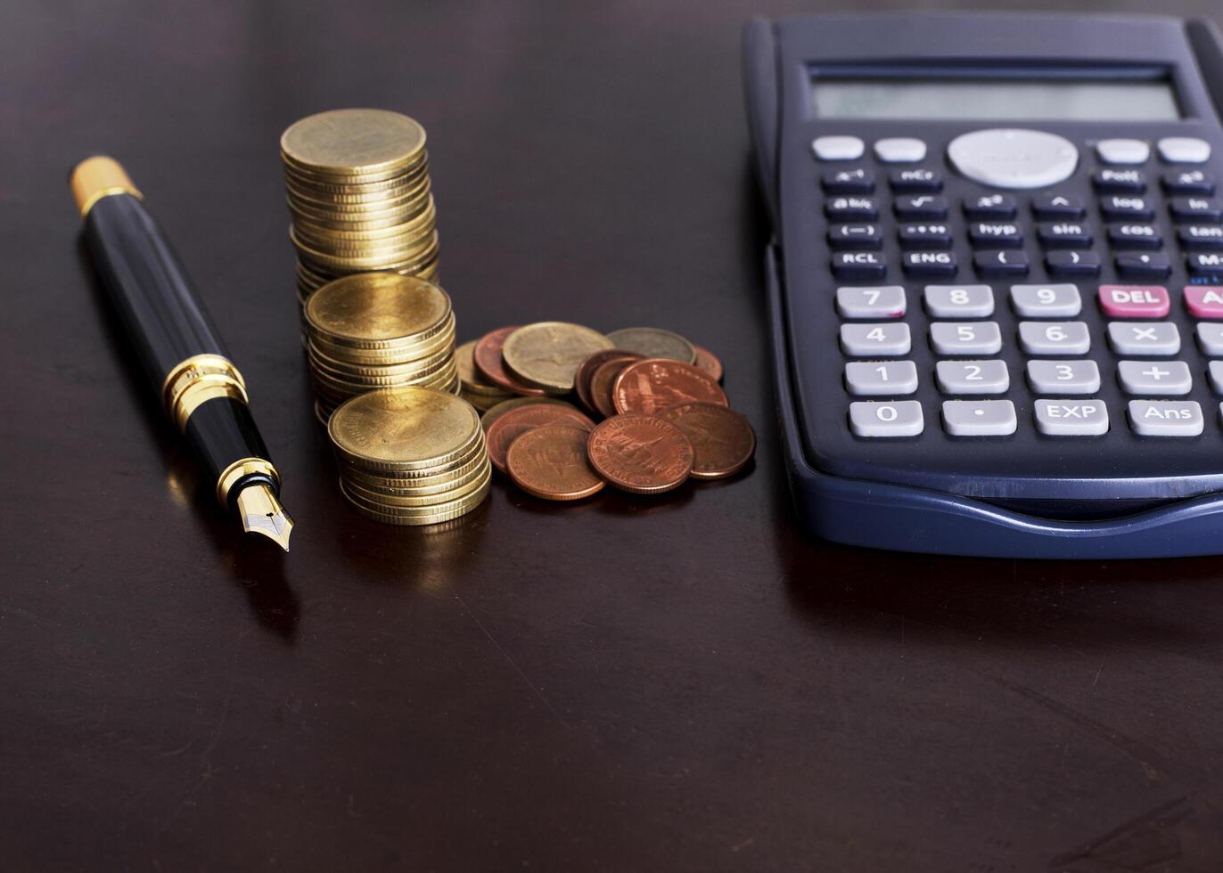 caneta-tinteiro, pilha de moedas e calculadora na mesa de madeira para o conceito de finanças foto