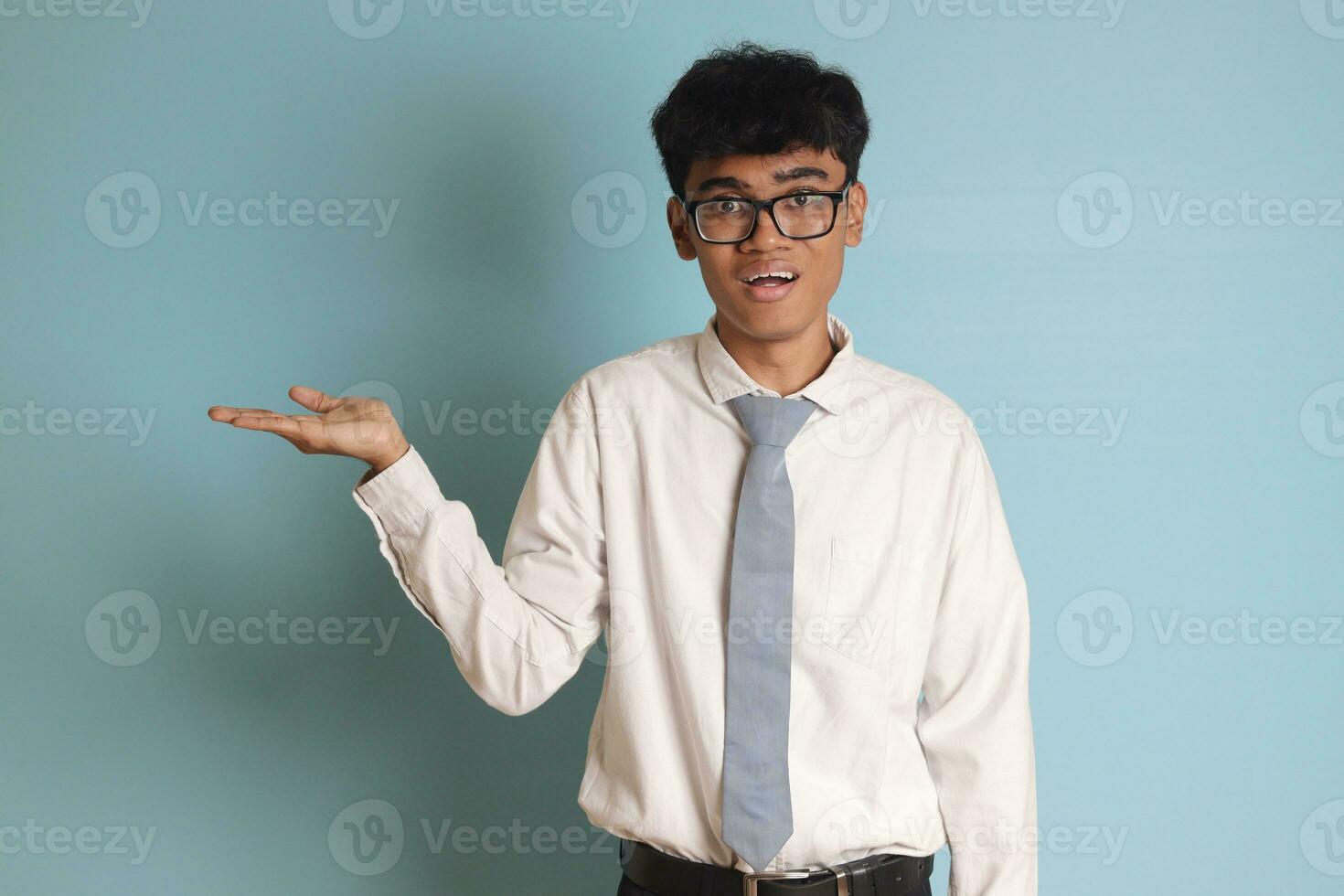 indonésio Senior Alto escola aluna vestindo branco camisa uniforme com cinzento gravata mostrando produtos, apontando às alguma coisa e sorridente. isolado imagem em azul fundo foto