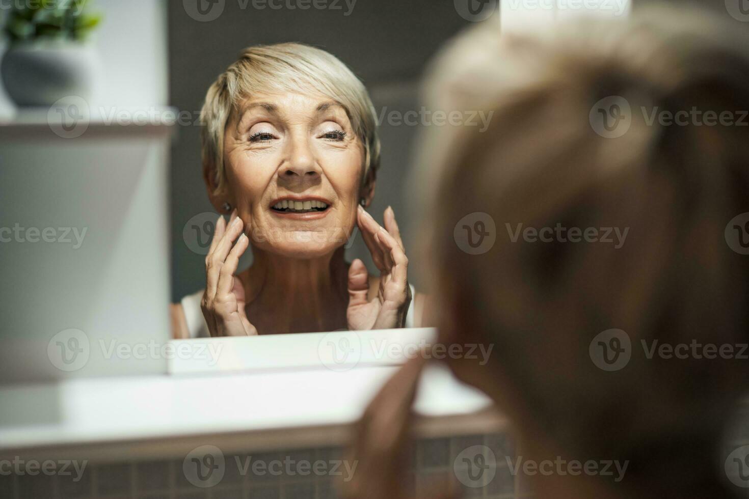 maduro mulher olhando às dela face dentro a banheiro. ela é examinando rugas em dela pele. foto
