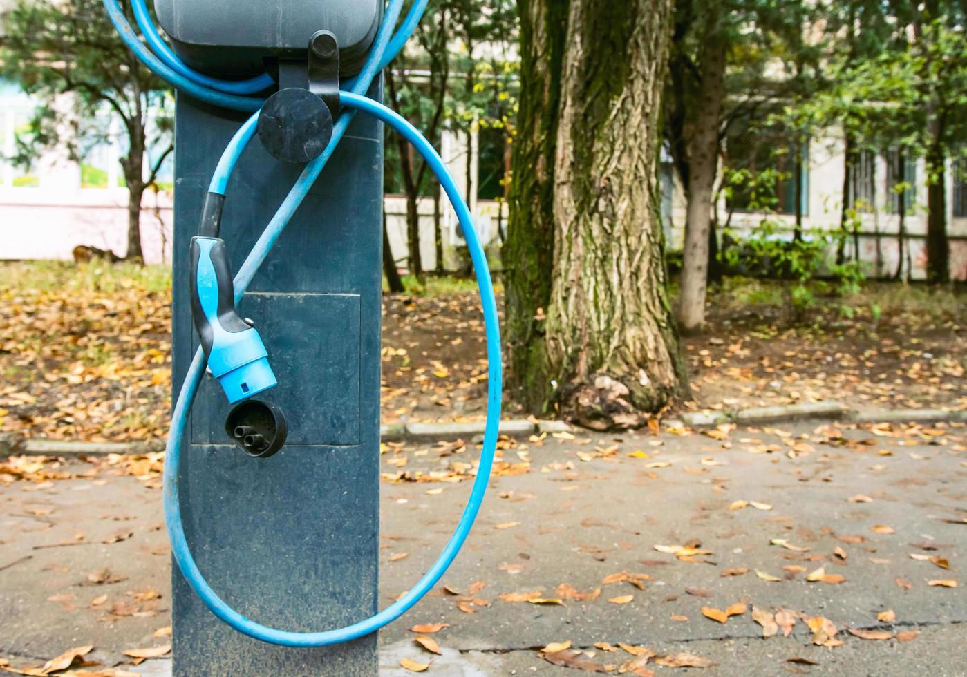 close-up da estação de carregamento de carro elétrico com mangueira solta e árvores ao fundo foto