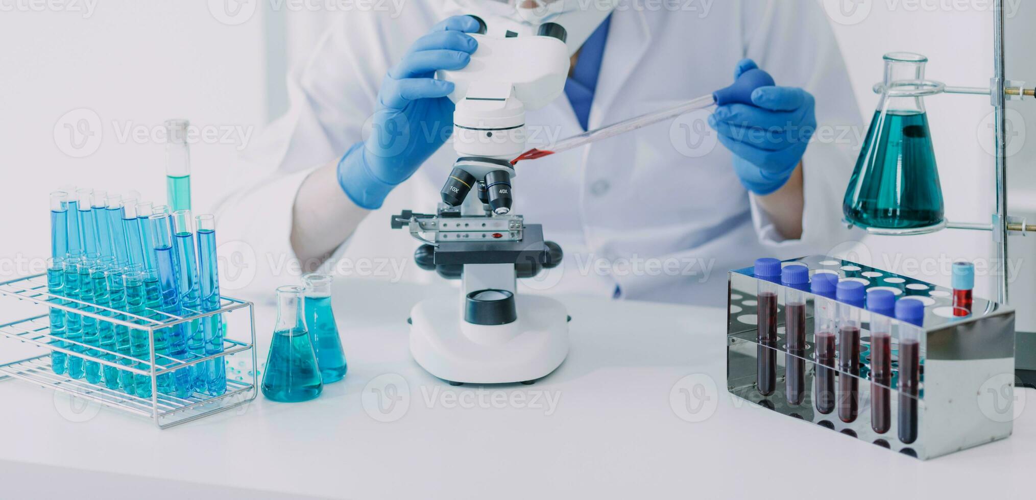 médico ou científico investigador pesquisando e experimentando multicolorido solução, frasco e microscópio dentro a laboratório ou dentro a laboratório de vestindo azul luvas e branco roupas completamente. foto