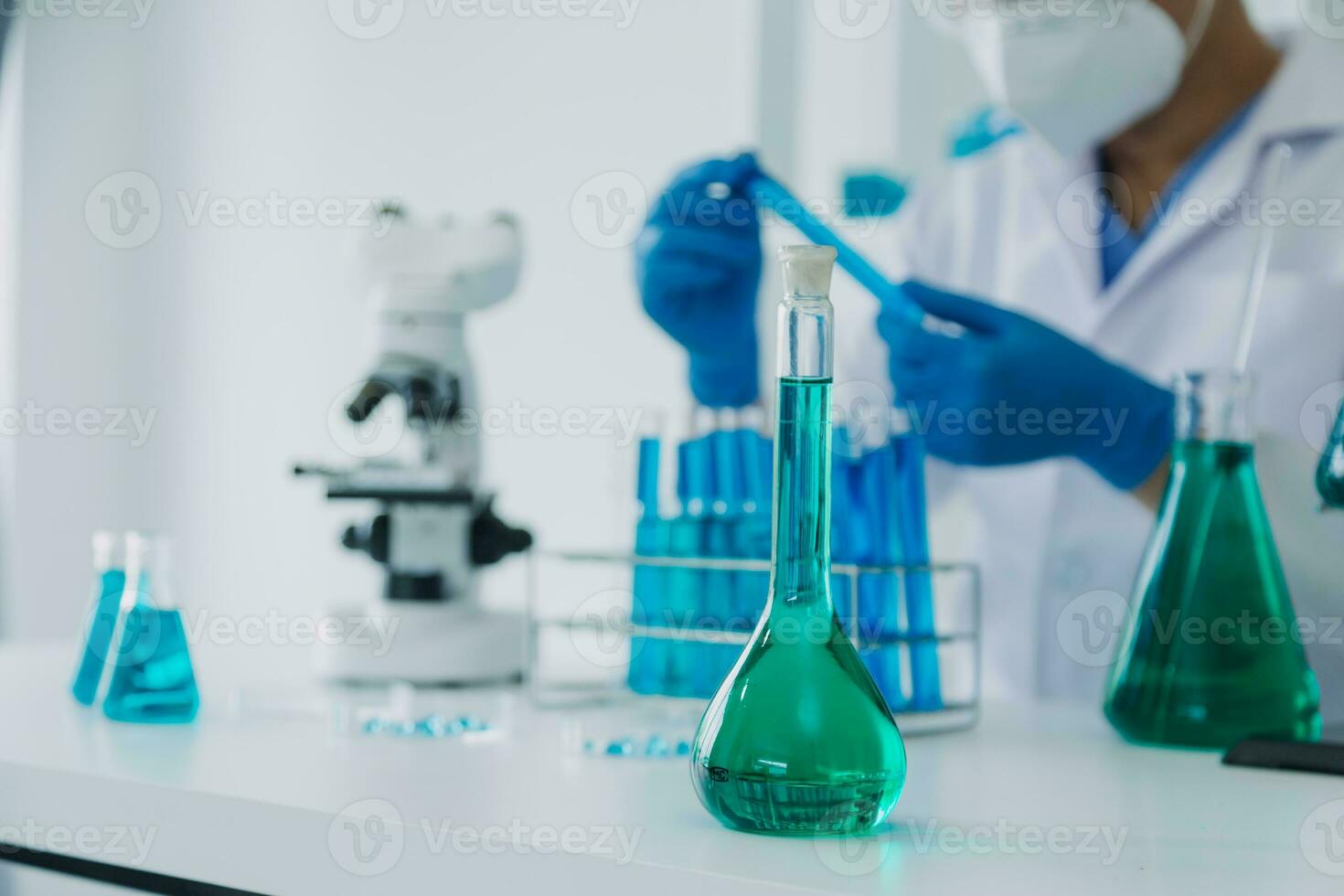 médico ou científico investigador pesquisando e experimentando multicolorido solução, frasco e microscópio dentro a laboratório ou dentro a laboratório de vestindo azul luvas e branco roupas completamente. foto