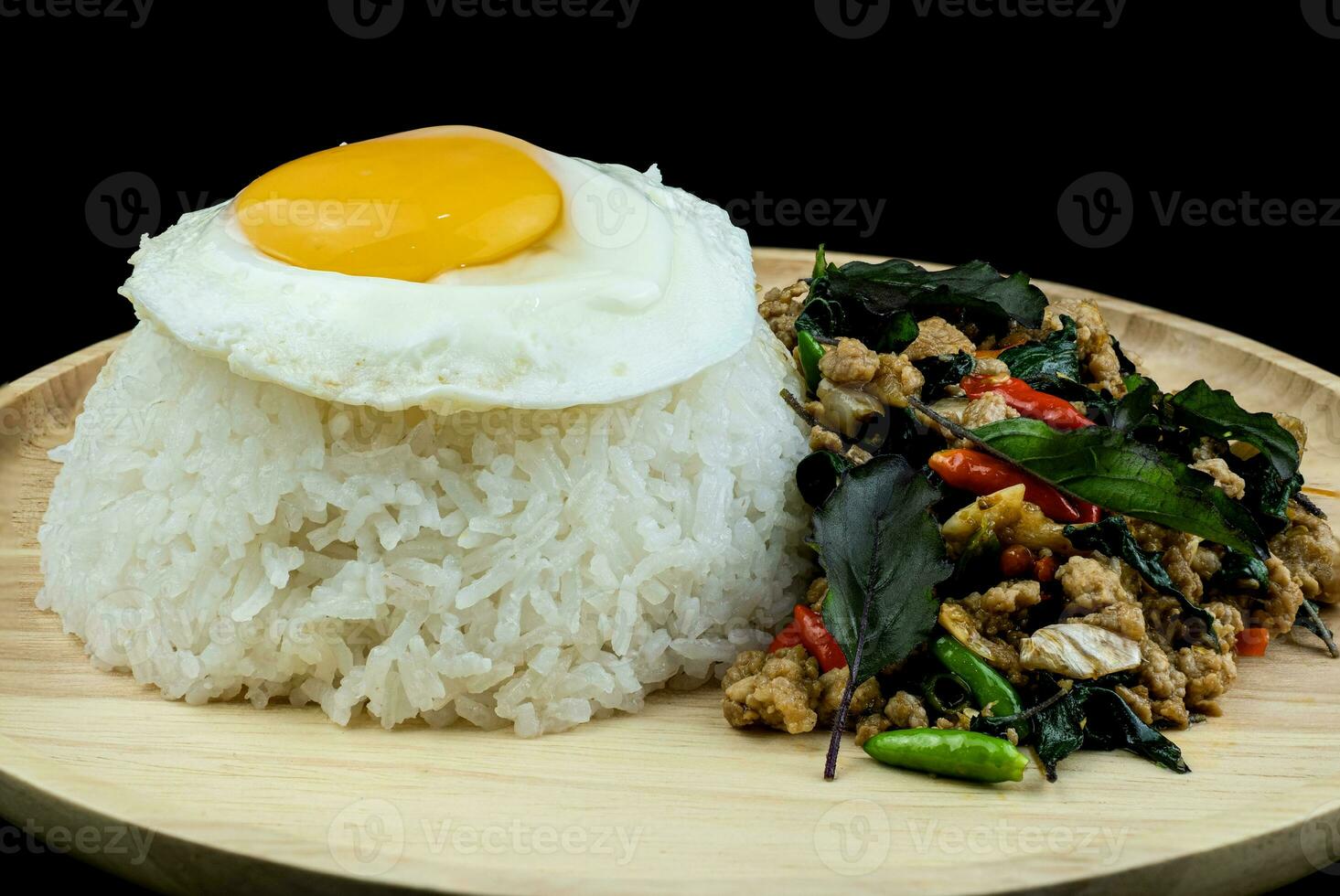 arroz com carne de porco frita picante com cobertura de folhas de manjericão, ovos fritos em um prato de madeira, pad krapow moo é comida tradicional tailandesa foto