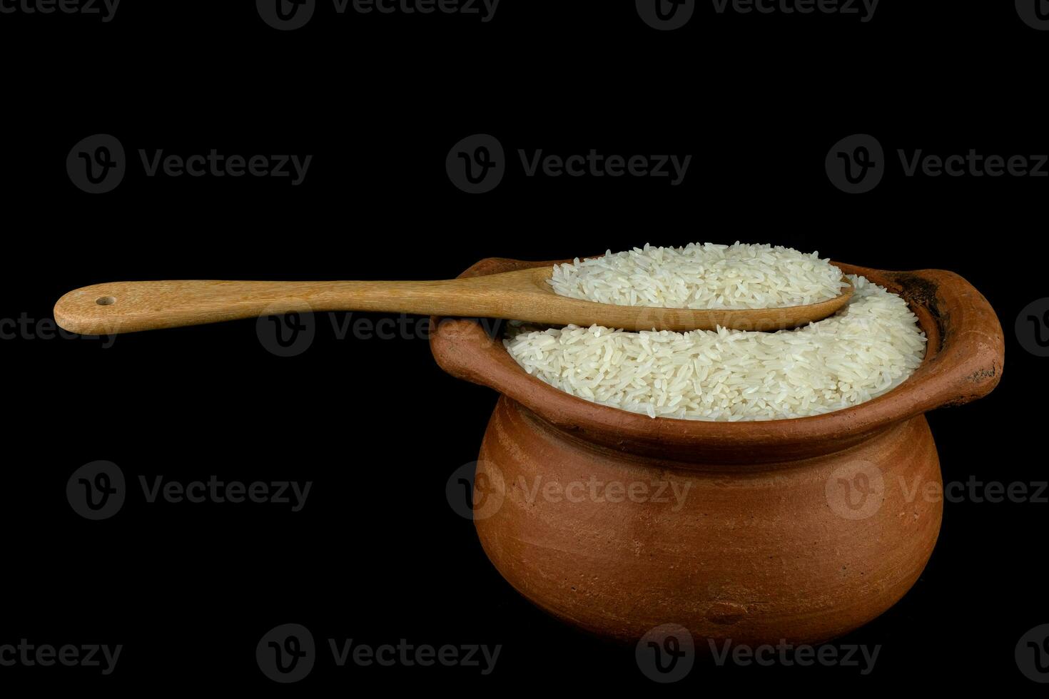 arroz de jasmim em uma panela de barro e uma concha de madeira isolada em um fundo preto foto