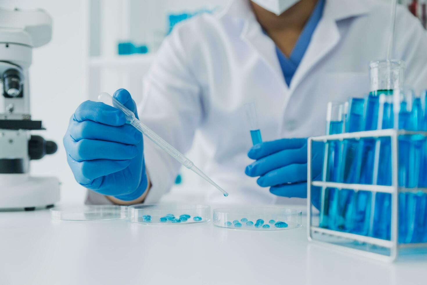 médico ou científico investigador pesquisando e experimentando multicolorido solução, frasco e microscópio dentro a laboratório ou dentro a laboratório de vestindo azul luvas e branco roupas completamente. foto