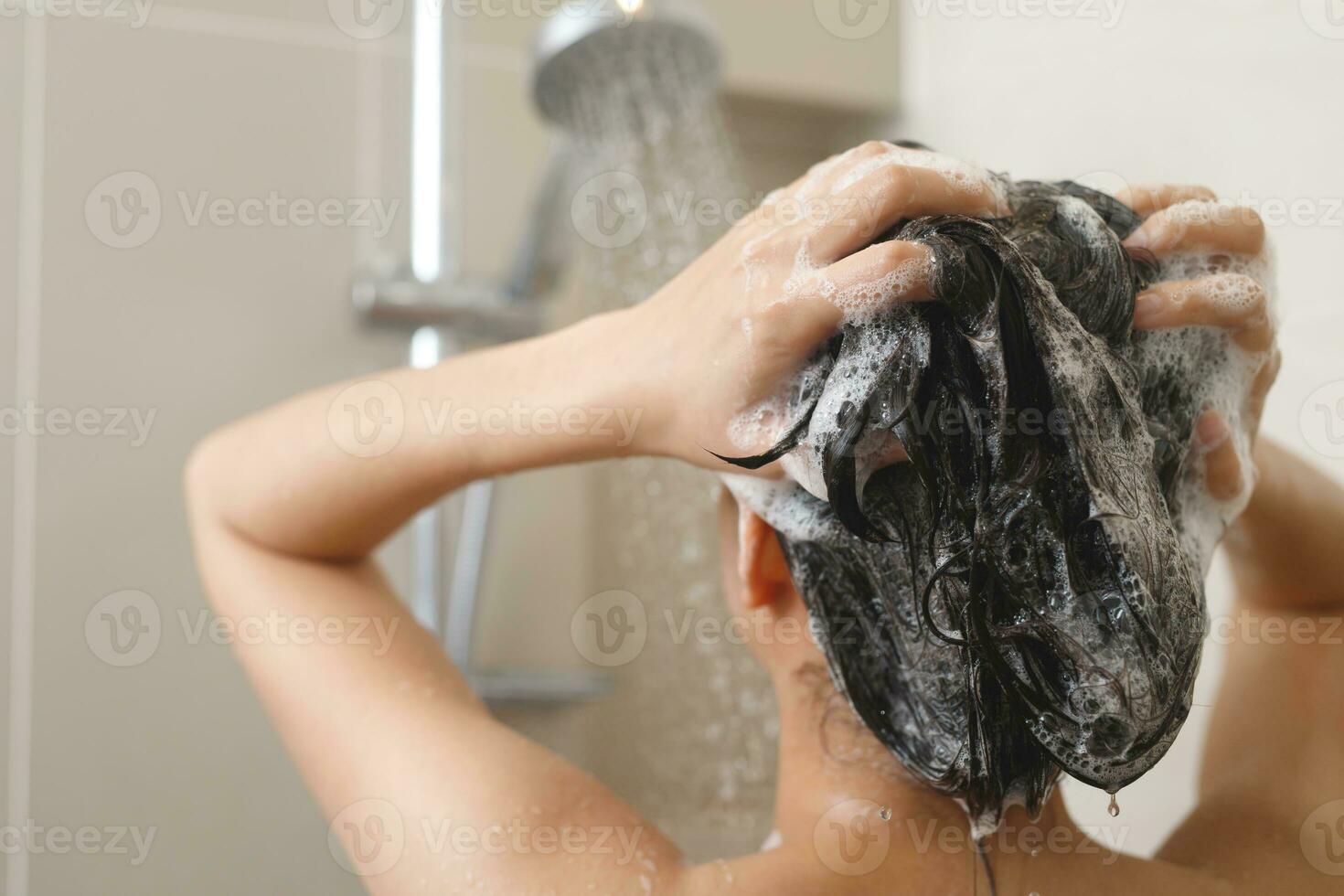 mulher levando chuveiro e lavando cabelo com xampu foto