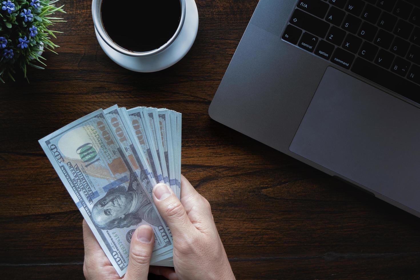 homem de negócios segurando a faixa do dólar com o laptop do computador da xícara de café e notebook na mesa de madeira no banco do escritório. foto