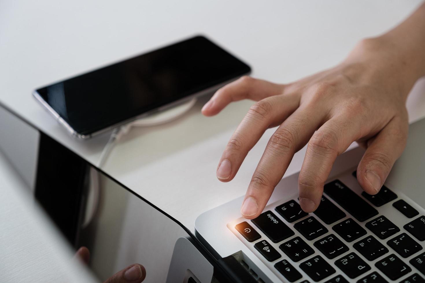 homem pressionando o botão liga / desliga em um computador laptop para desligar o smartphone, desconexão de mídia social e proibição de tecnologia, conceito de desintoxicação digital. foto