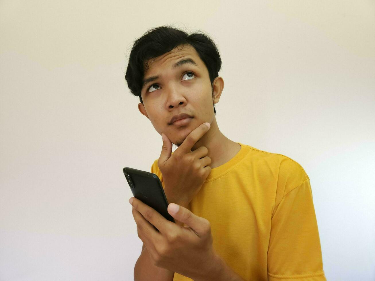 ásia homem segurando Móvel telefone olhando acima às cópia de espaço foto