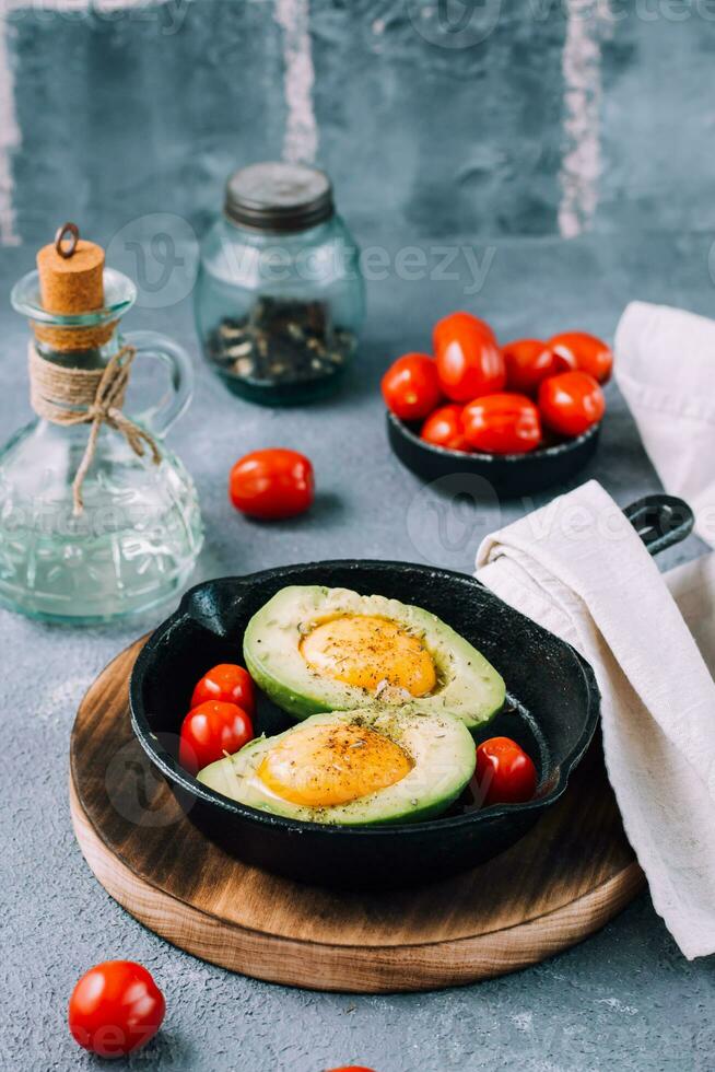 cru abacate metades, pronto para assar, recheado com ovo e cereja tomates dentro uma panela em a mesa. saudável comendo. flexitarista dieta. vertical Visão foto