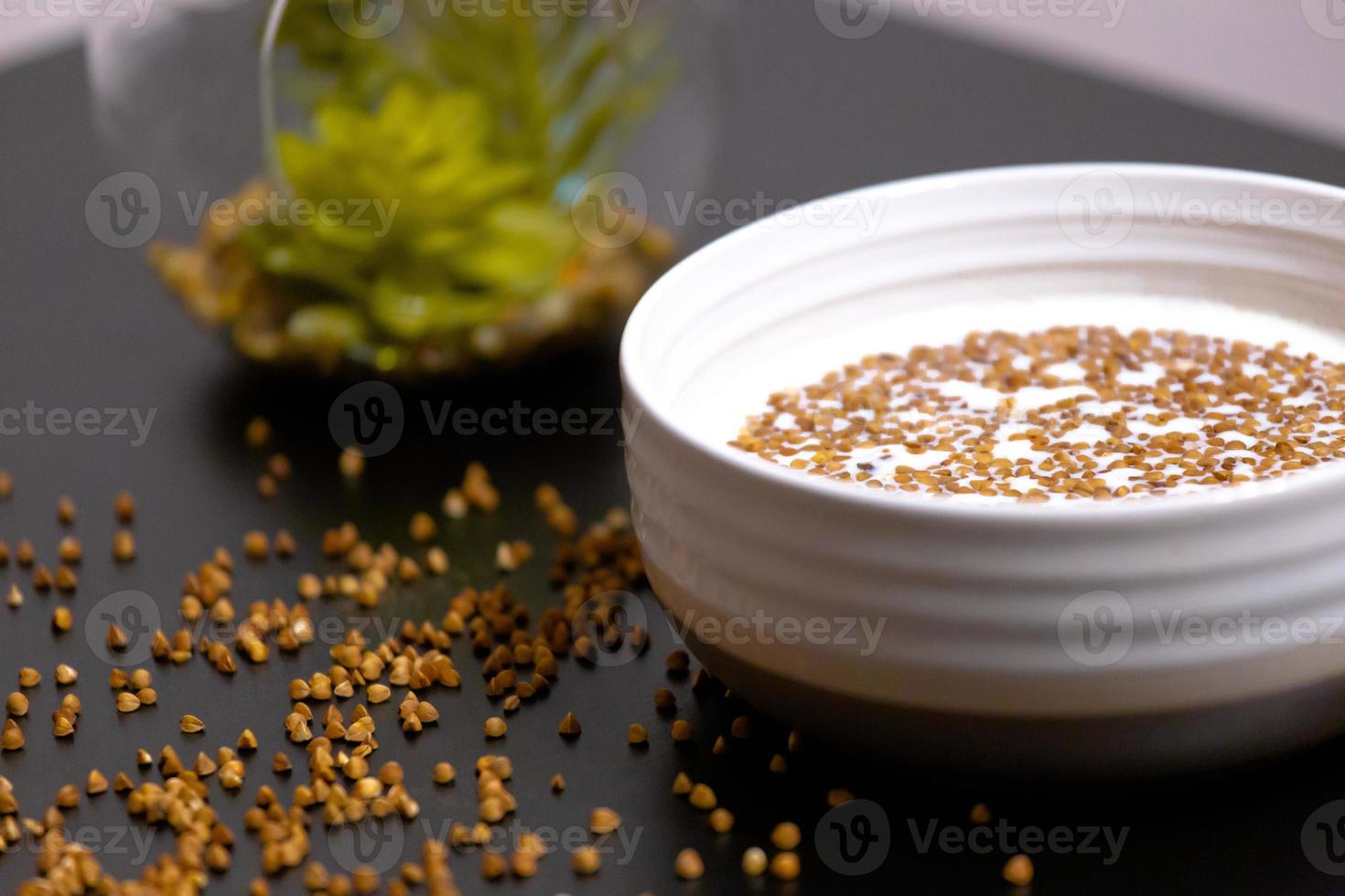 alimentação saudável mingau de trigo sarraceno em um prato cheio de leite em uma mesa escura com verduras foto