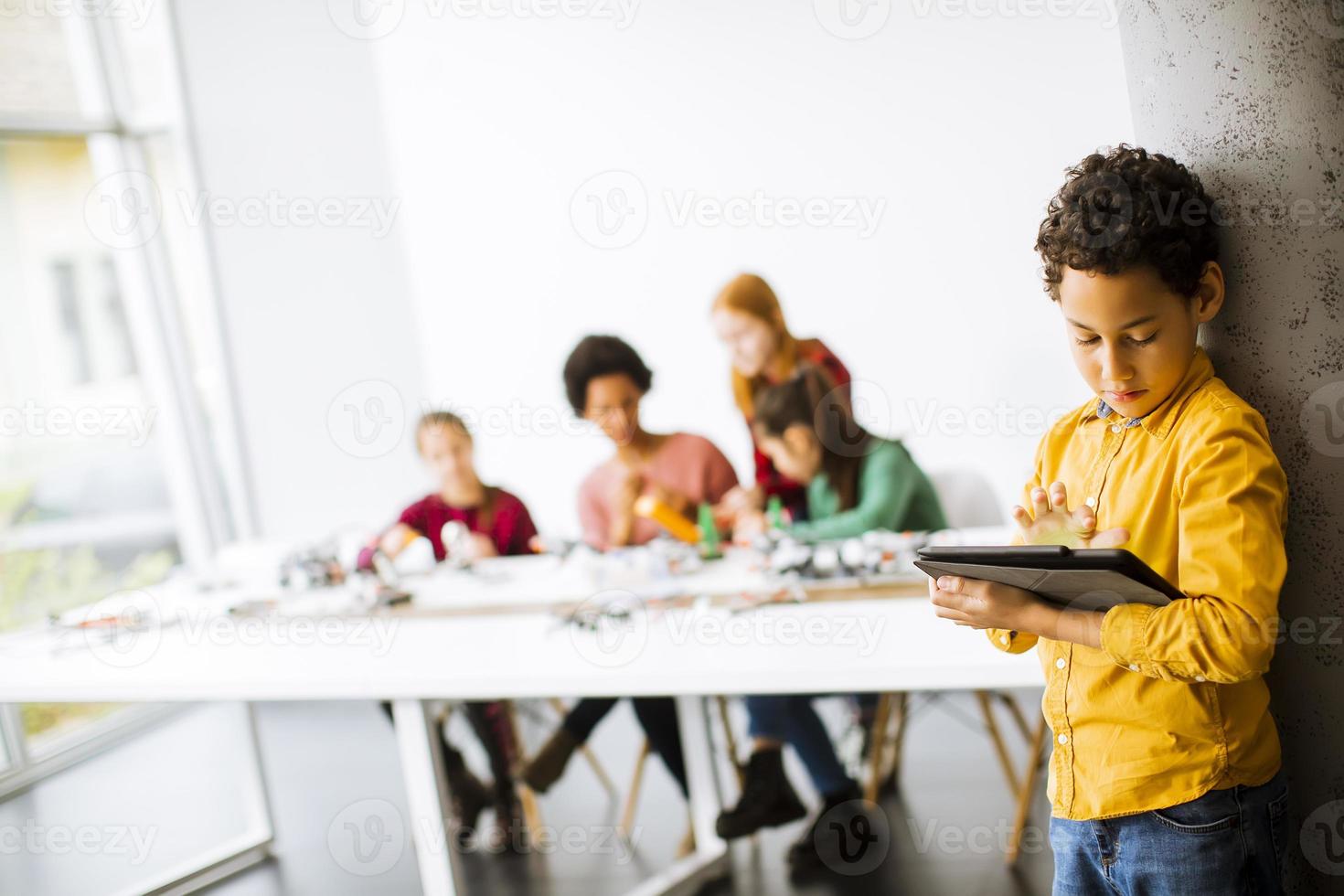garotinho fofo em frente a crianças programando brinquedos elétricos e robôs na sala de aula de robótica foto
