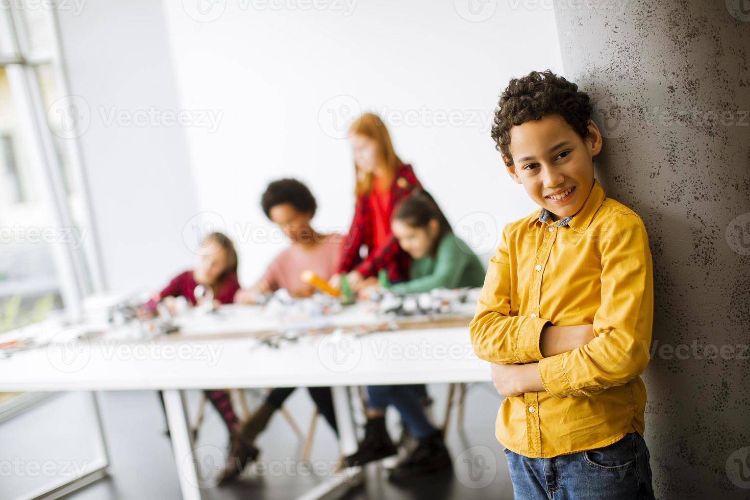 garotinho fofo em frente a crianças programando brinquedos elétricos e robôs na sala de aula de robótica foto