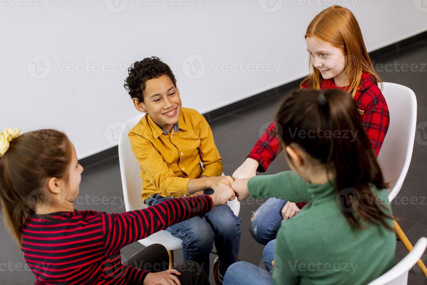 retrato de crianças fofas em jeans conversando e sentando em cadeiras contra uma parede branca foto