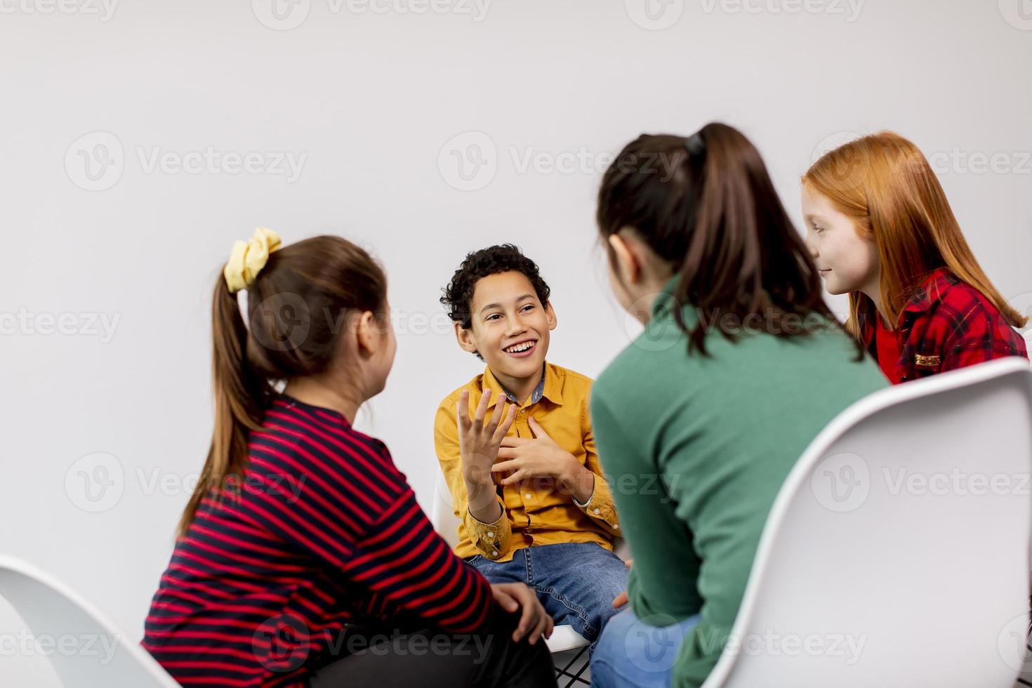 retrato de crianças fofas em jeans conversando e sentando em cadeiras contra uma parede branca foto