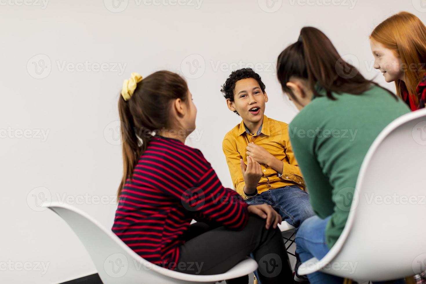 retrato de crianças fofas em jeans conversando e sentando em cadeiras contra uma parede branca foto