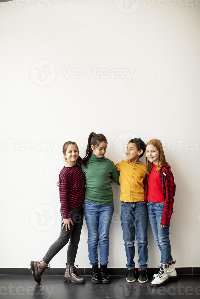 retrato de crianças fofas em jeans olhando para a câmera e sorrindo em pé contra uma parede branca foto