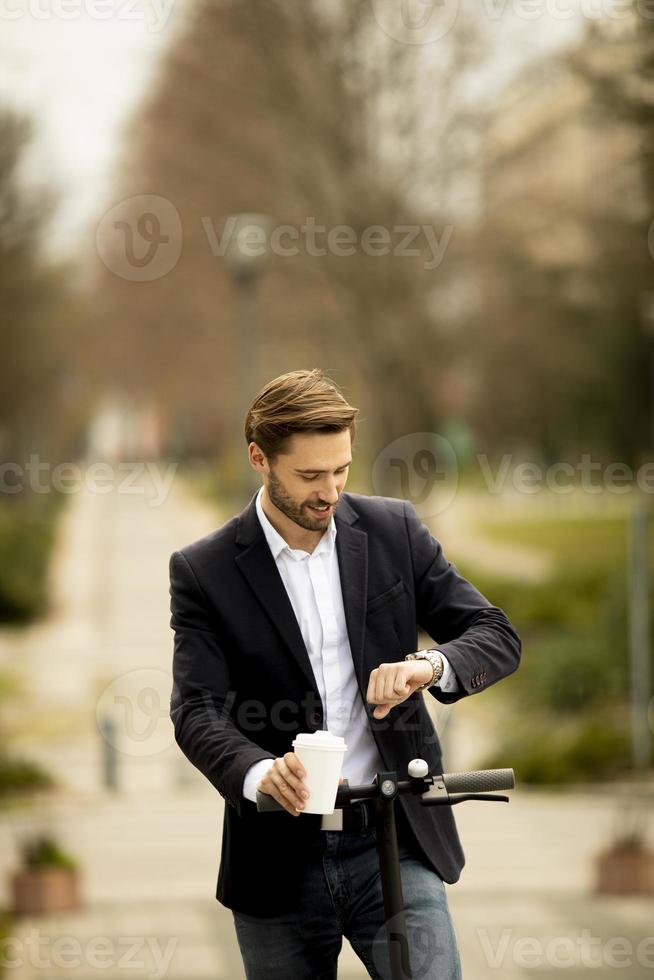 jovem empresário com xícara de café para viagem e verificando o tempo na scooter elétrica foto