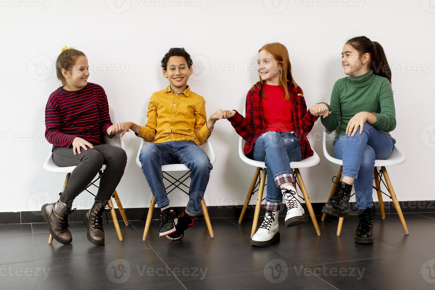 retrato de crianças fofas em jeans, sentadas em cadeiras contra uma parede branca foto