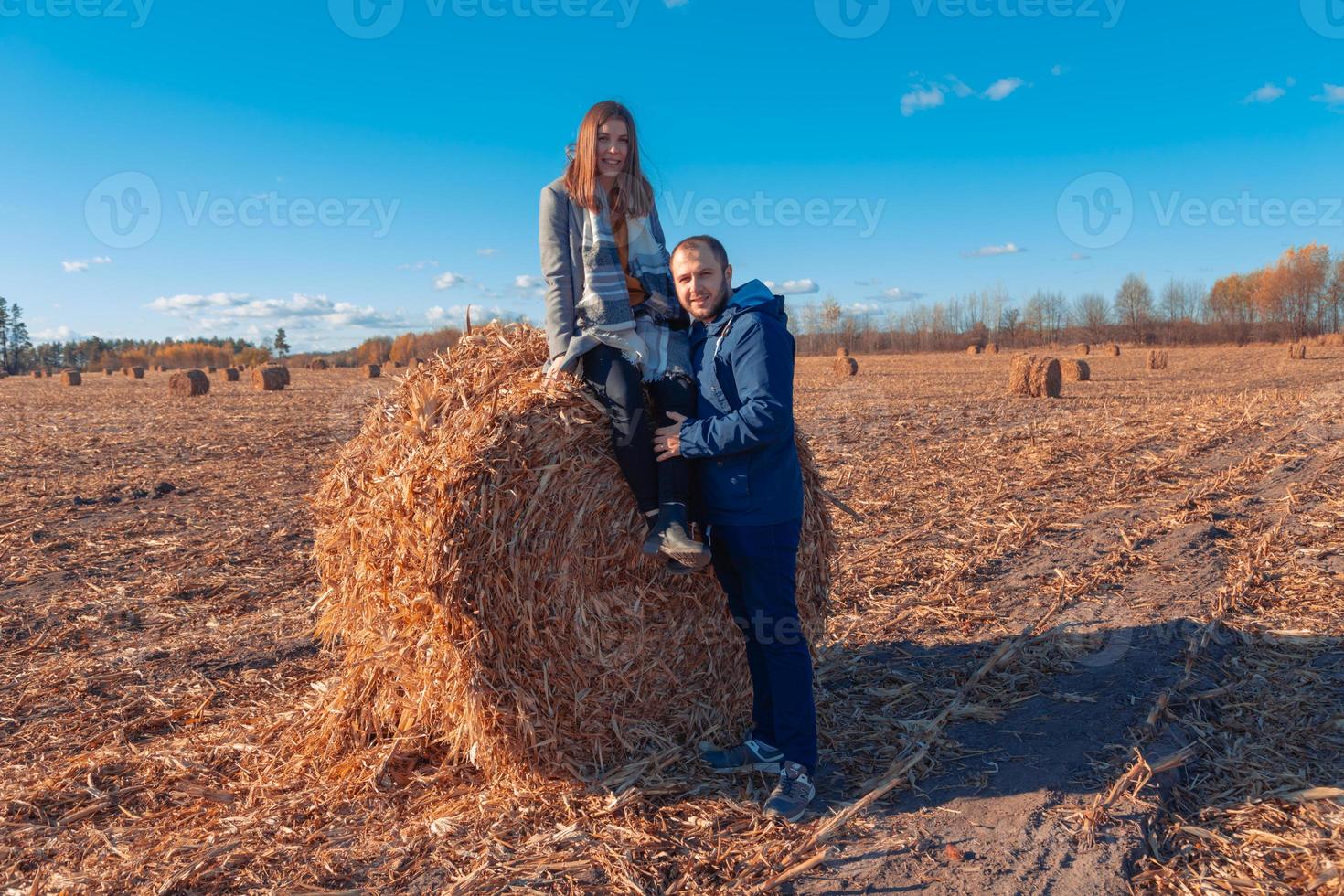 uma garota e um cara estão perto de um grande fardo com feno em um campo e um céu azul foto