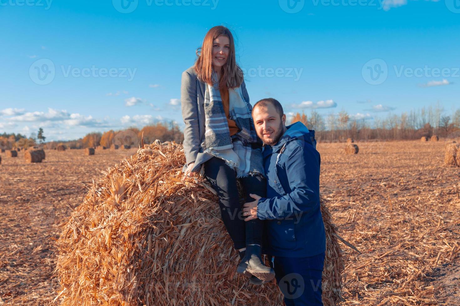 uma garota e um cara estão perto de um grande fardo com feno em um campo e um céu azul foto