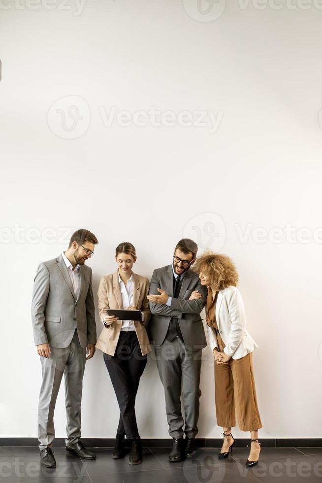 empresários multiétnicos usando tablet digital em pé junto à parede no escritório foto