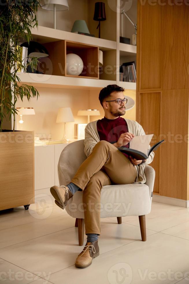 jovem bonito com roupas casuais e óculos lendo um livro foto