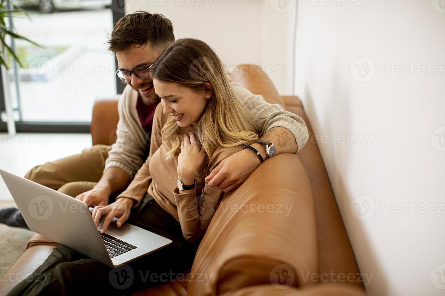 jovem casal usando laptop juntos enquanto está sentado no sofá em casa foto