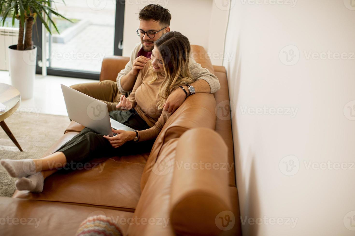 jovem casal usando laptop juntos enquanto está sentado no sofá em casa foto