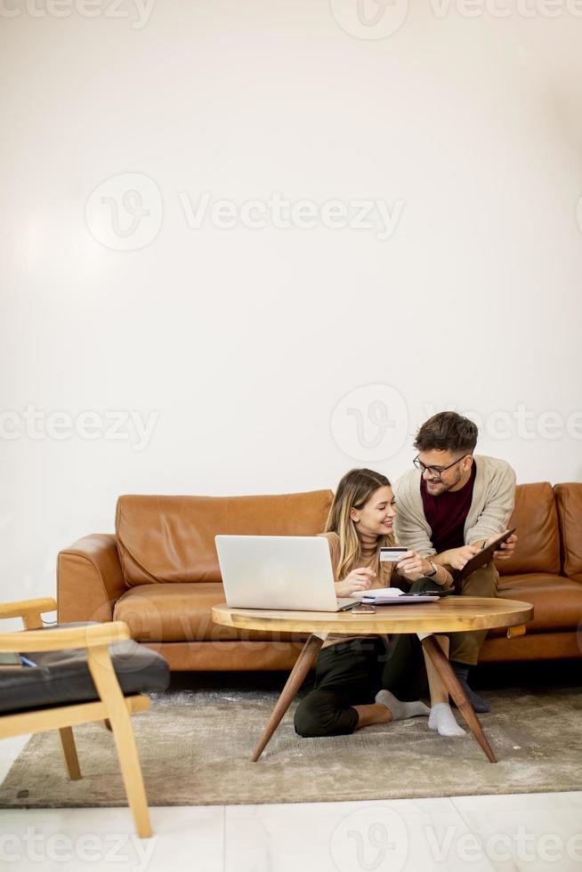 mulher e homem jovem usando laptop para pagamento on-line enquanto estão sentados no sofá em casa foto