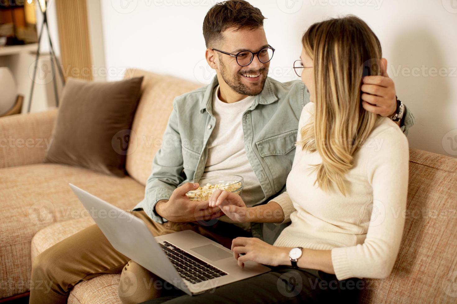 jovem casal usando laptop juntos enquanto está sentado no sofá em casa foto