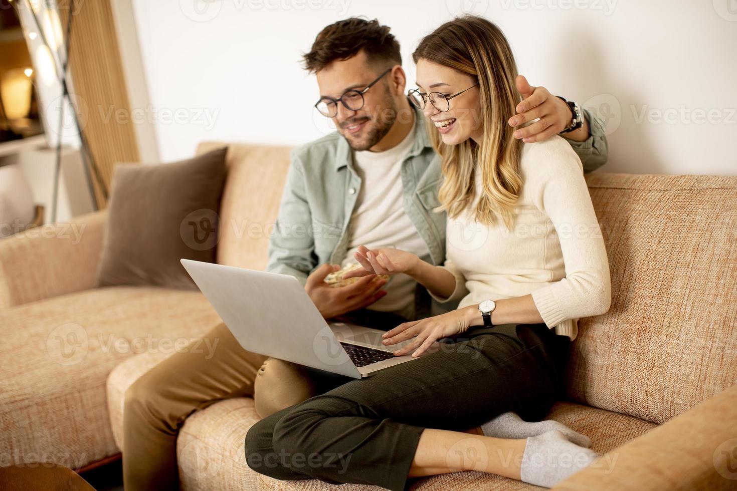 jovem casal usando laptop juntos enquanto está sentado no sofá em casa foto