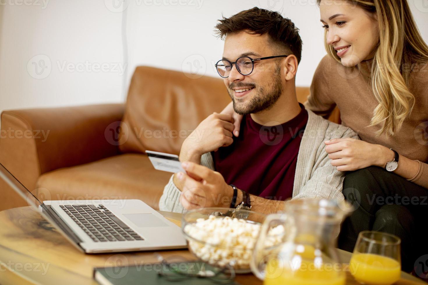 mulher e homem jovem usando laptop para pagamento on-line enquanto estão sentados no sofá em casa foto