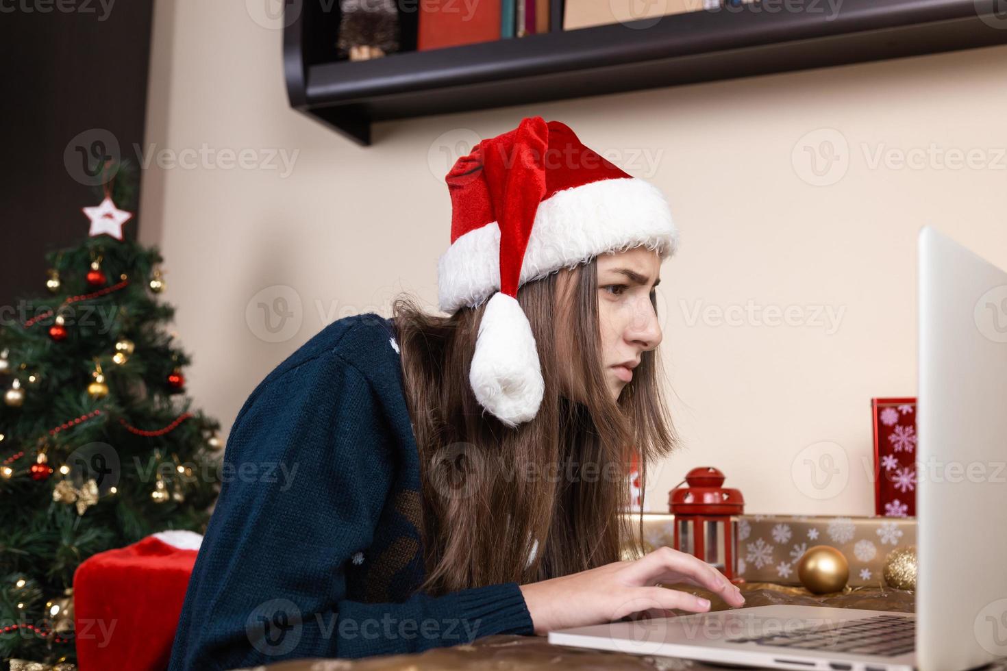 menina com chapéu de Papai Noel usando laptop para videochamada para amigos e pais foto