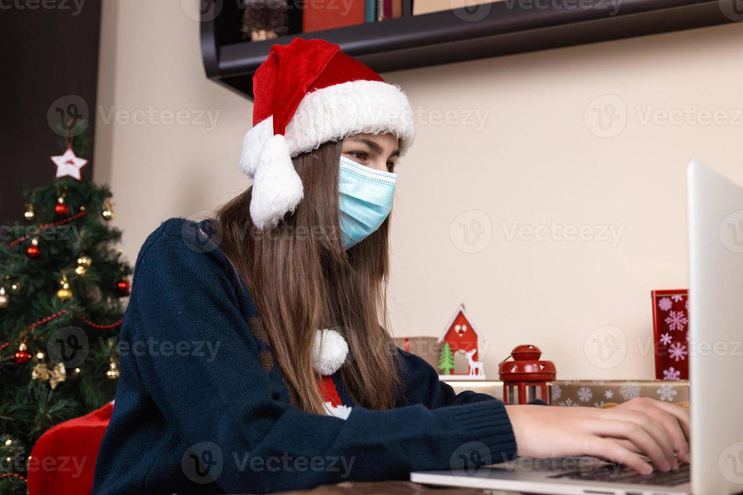 menina com chapéu de Papai Noel usando laptop para videochamada para amigos e pais foto