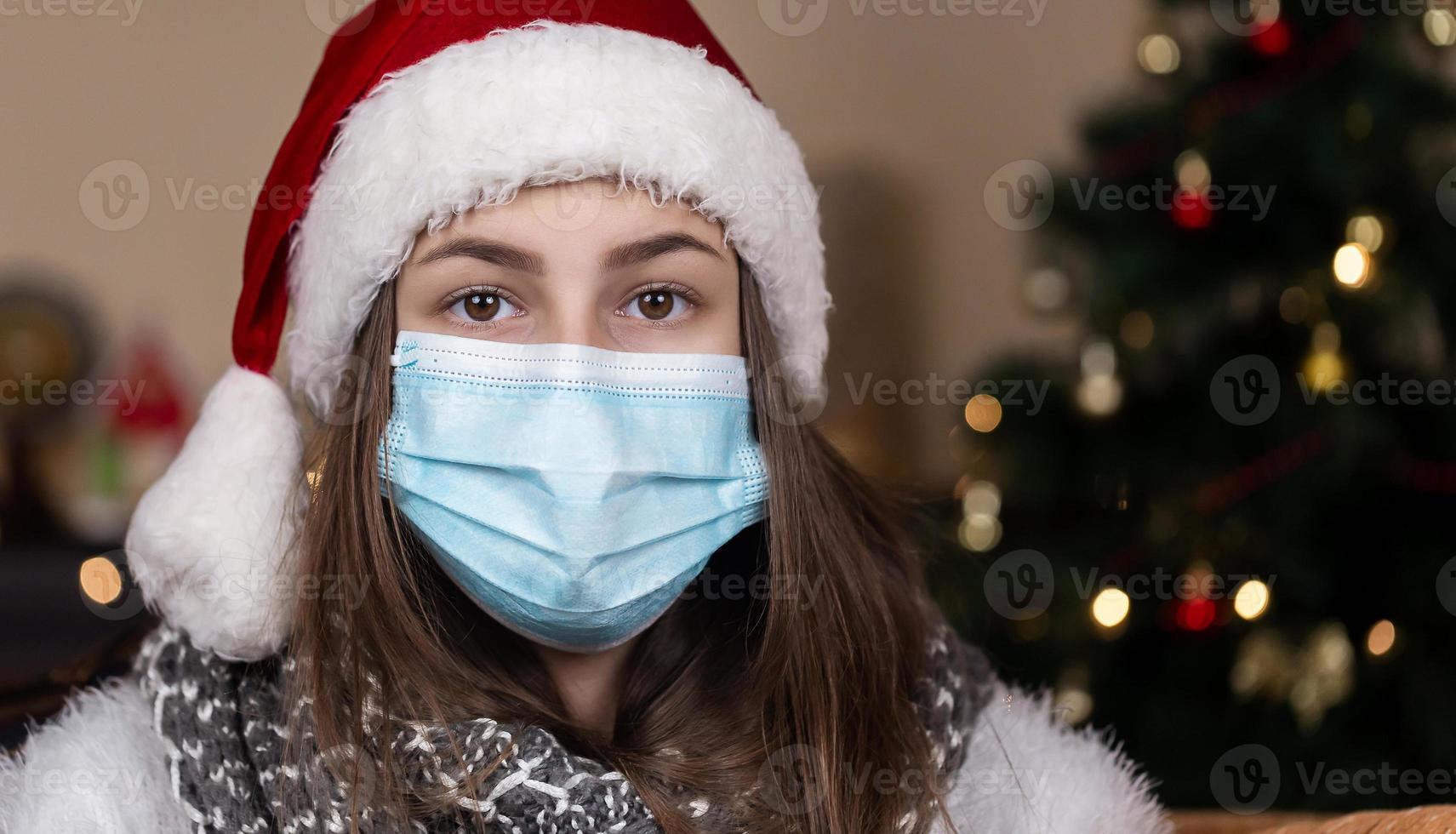 retrato de uma jovem adolescente com chapéu de Natal de Papai Noel vermelho e máscara médica foto