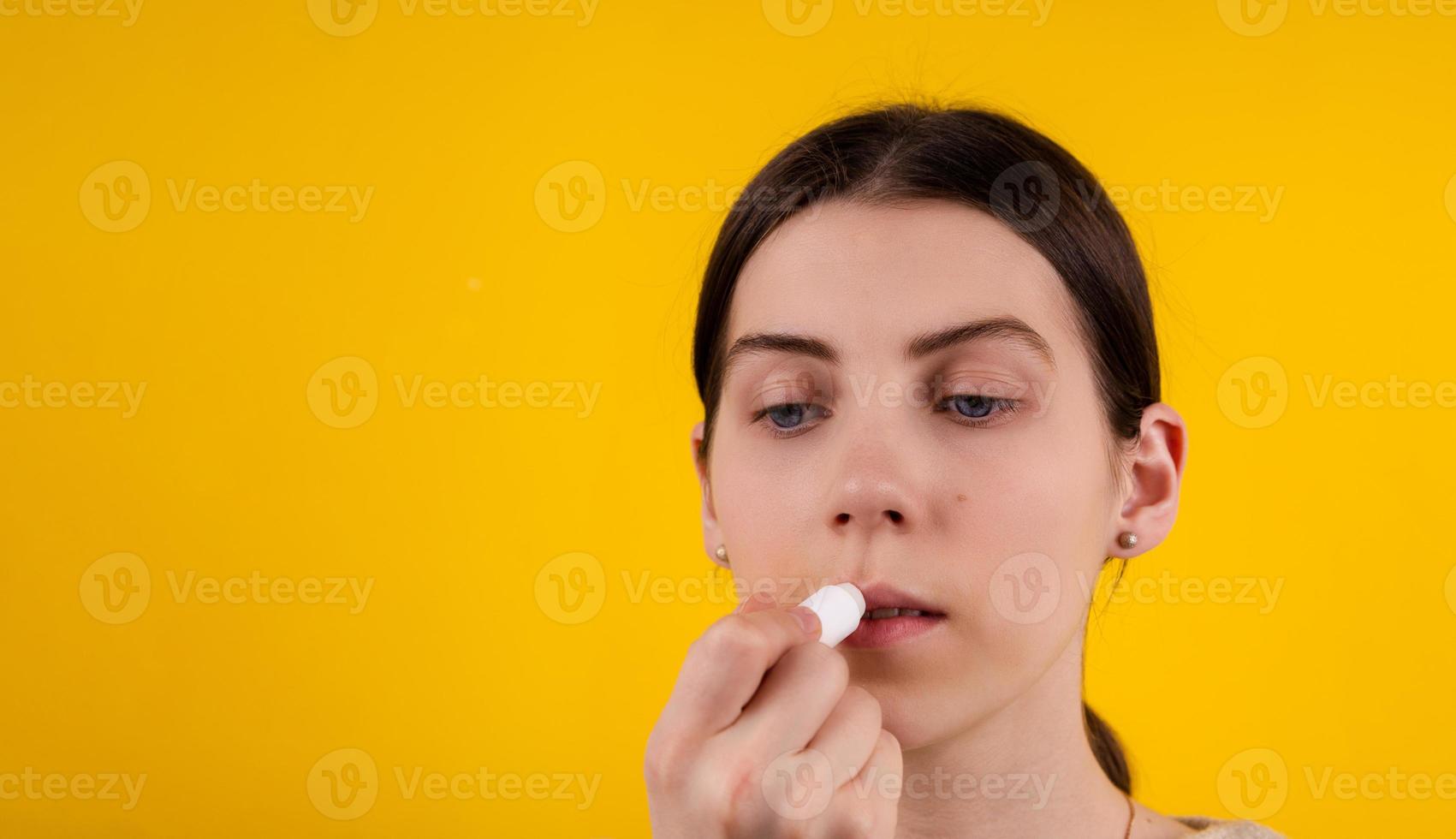 mulher jovem e atraente usando batom higiênico em fundo amarelo foto