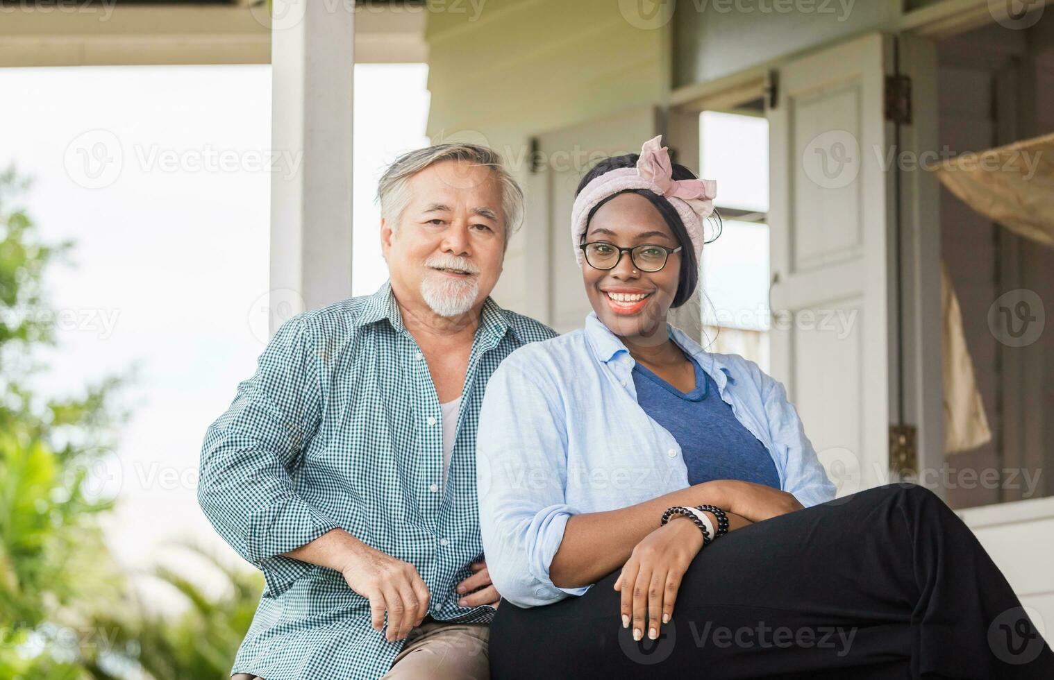 alegre mulher afro-americana e homem asiático sênior sentado relaxa no terraço e olhando para a câmera foto