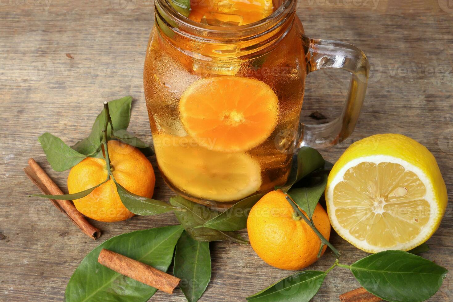 líquido gelo limão laranja chá com fatia verde folha canela bastão dentro transparente vidro jarra caneca em rústico madeira fundo todo fruta foto