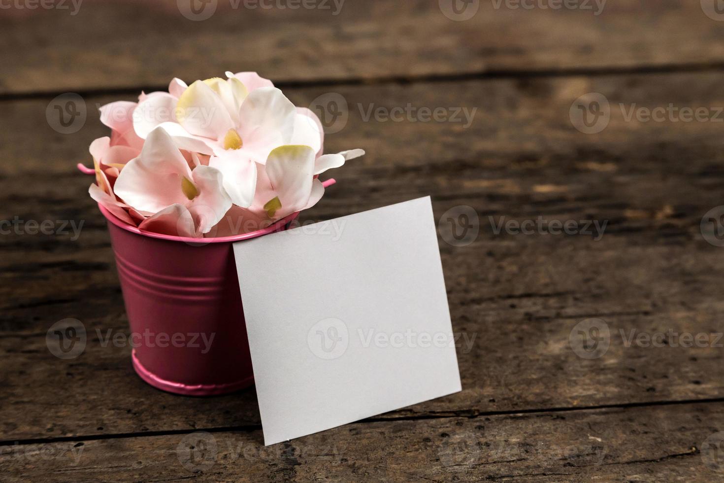 flores de hortênsia rosa pastel em um pequeno balde e um pedaço de papel no fundo de madeira foto