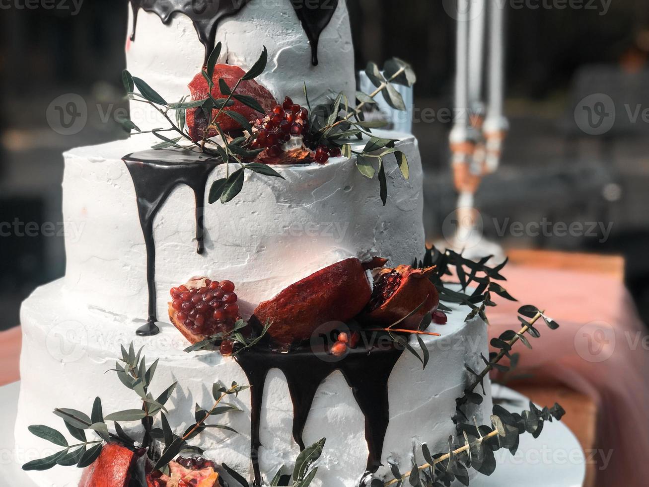 lindo bolo de casamento de creme branco de três camadas com frutas da romã e flores frescas na mesa e velas foto