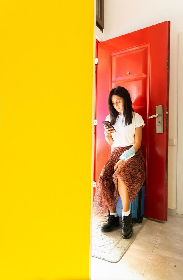 garota parada na porta com telefone e bagagem foto