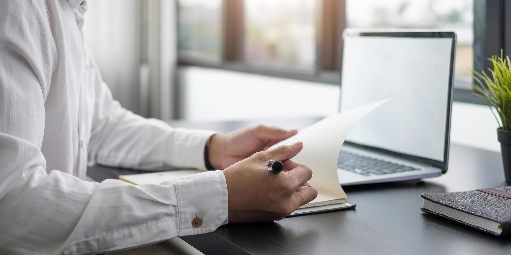 planejamento de negócios homem de negócios escrevendo no caderno e trabalhando no computador laptop no escritório moderno homem estudando curso on-line via laptop e palestra no bloco de notas foto