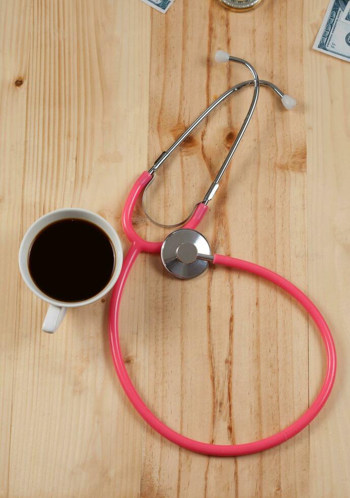 Rosa estetoscópio é médico instrumentos com quente café em de madeira. foto